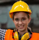 Young technician in a yellow hard hat with ear defenders around her neck