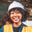Smiling technician with curly hair in a white hard hat and orange vest